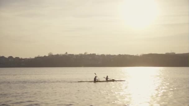 Silhuetten av två person paddling i havet vid solnedgången — Stockvideo