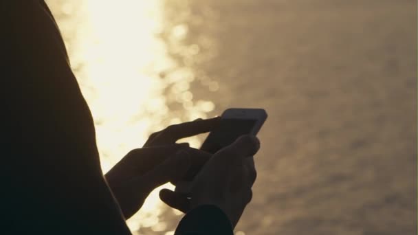Hombre usando el teléfono celular al aire libre contra un fondo de luz solar fulgurante al atardecer - primer plano . — Vídeo de stock
