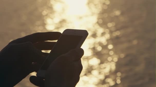 Silueta del hombre que usa el teléfono inteligente al lado del depósito con puesta de sol - cámara lenta — Vídeo de stock