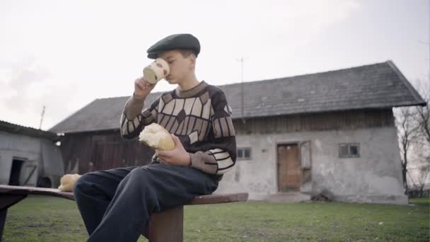 Głodny chłopiec spożywa bochenek chleba i pije mleko — Wideo stockowe