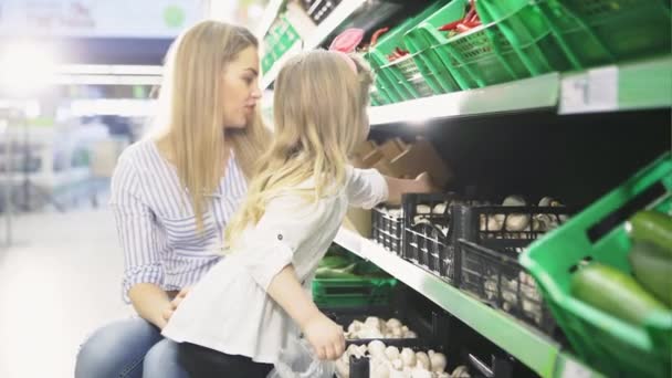 Vrouw met haar jonge dochter champignon kiezen in een markt van groenten — Stockvideo