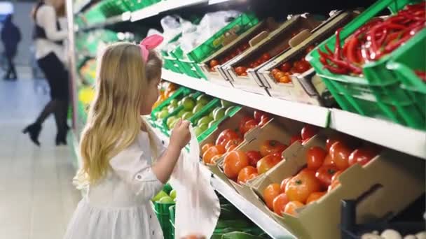 Menina bonito está pegando pacote de tomate de uma prateleira no departamento de legumes em um supermercado — Vídeo de Stock