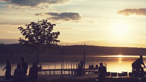 Menschen in der Stadt ruhen sich am See vor dem Hintergrund eines schönen Sommersonnenuntergangs aus — Stockvideo