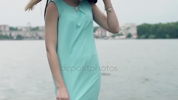 Menina bonita posando na frente da câmera no fundo do rio e da cidade. Olha para a câmara. Movimento lento — Vídeo de Stock