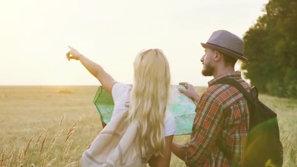Glücklich reisende junge Leute wählen eine Route auf der Landkarte vor dem Hintergrund des Sonnenaufgangs in einem weitläufigen Feld. — Stockvideo