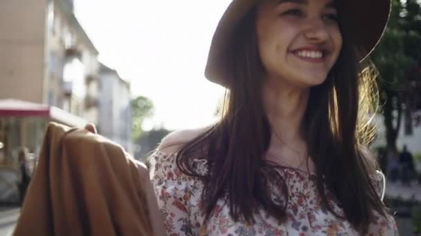 Schöne glückliche Mädchen in einem Hut, die durch die Straßen der Stadt vor dem Hintergrund einer strahlenden Sonne. — Stockvideo