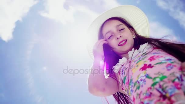 Portrait of joyful little girl in a hat against the blue sky. Sunny morning in the park. Back light, low point of shooting. — Stock Video