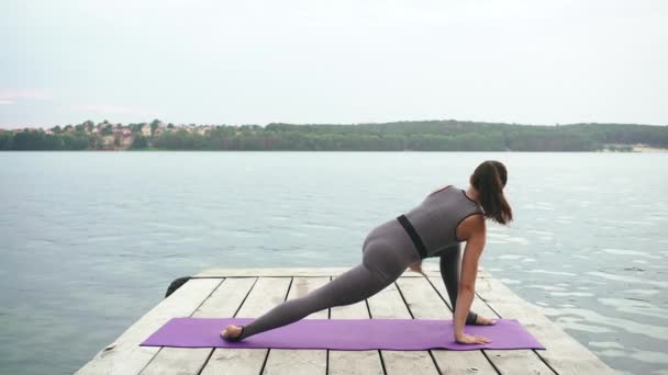 Fit woman stretching on pier by water — Stock Video