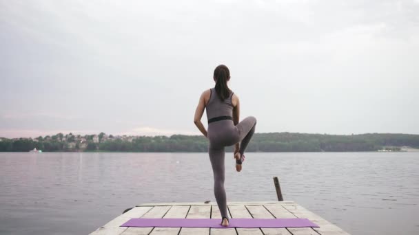 Μια νεαρή γυναίκα με ένα λεπτό σχέδιο ασχολείται με την γυμναστική στη θάλασσα - Utthita Hasta Padangusthasana — Αρχείο Βίντεο