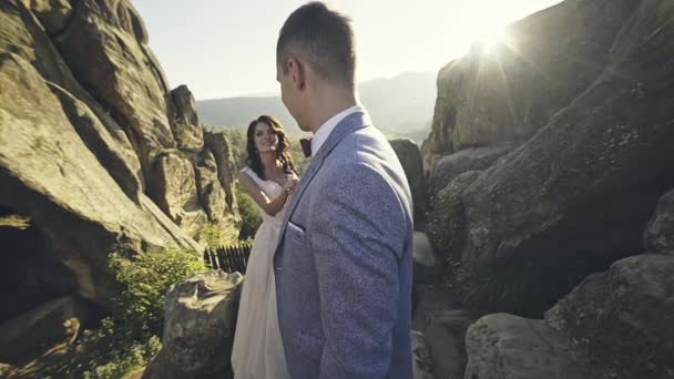 Dos amantes tienen un beso recién besado en el fondo de grandes rocas y puesta de sol — Vídeos de Stock