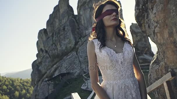 Eine geheimnisvolle schöne Braut mit Augenbinde erwartet ihren Verlobten vor dem Hintergrund des Sonnenuntergangs zwischen den magischen Felsen — Stockvideo