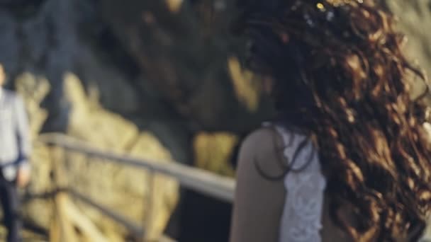 Een mooie vrouw in een bioloum jurk leidt met vertrouwen naar haar geliefde man tegen de achtergrond van de rotsen en de zomer zonsondergang. — Stockvideo