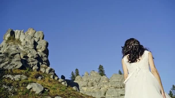 Gelukkige bruid tegen de achtergrond van zuivere blauwe hemel springt en cirkels voor plezier. Prachtige trouwjurk en kapsel. — Stockvideo