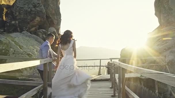 Весільна пара щасливо біжить, тримаючи руки в горах з приголомшливими видами — стокове відео