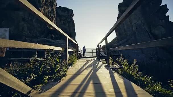 Magiska möte av brudar på en träbro mellan höga klipporna på bakgrunden av solnedgången. — Stockvideo