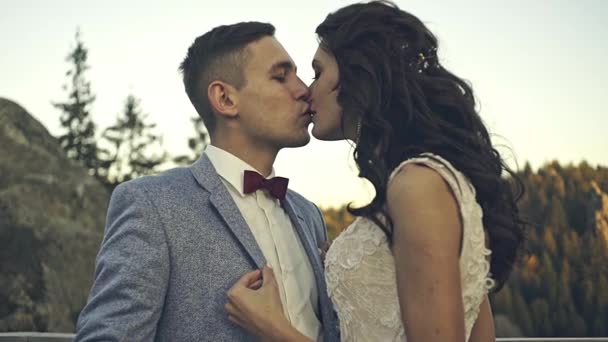 Evening sun illuminates the rocks where wedding couple kisses — Stock Video