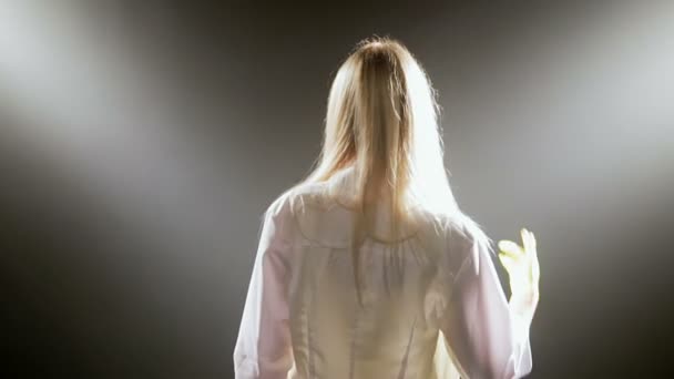 Девушка в белом халате показывает указательный палец на черном фоне . — стоковое видео