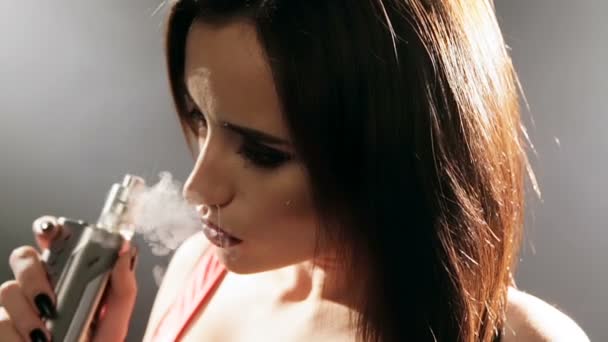 Uma mulher bonita fuma cigarros eletrônicos em um fundo cinza em um estúdio — Vídeo de Stock