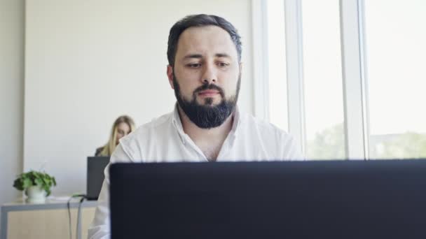 Joven empleado mirando el monitor de la computadora durante la jornada laboral en la oficina — Vídeo de stock