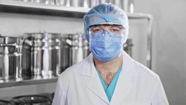 Portrait d'un travailleur de la santé dans un masque et des lunettes de protection sur le fond d'un rack avec des ustensiles métalliques . — Video