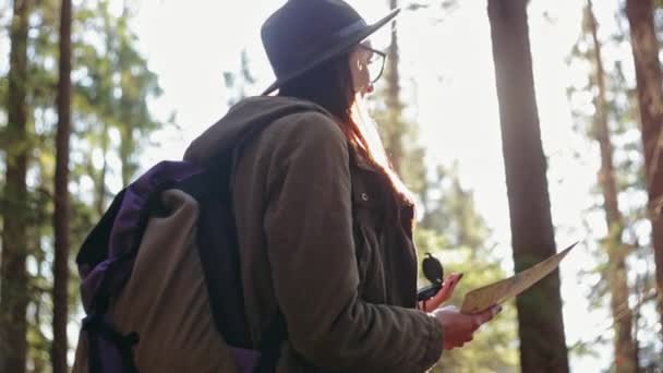 Stylish traveler girl in hat looking at map, exploring woods. — Stock Video