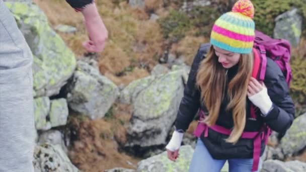 Mujer bonita mochilero senderismo en las montañas se le da una mano de ayuda desde arriba por su novio sonriente — Vídeo de stock