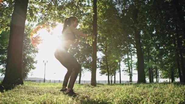 Femme active faisant squats tout en faisant de l'exercice dans le parc par une journée ensoleillée . — Video