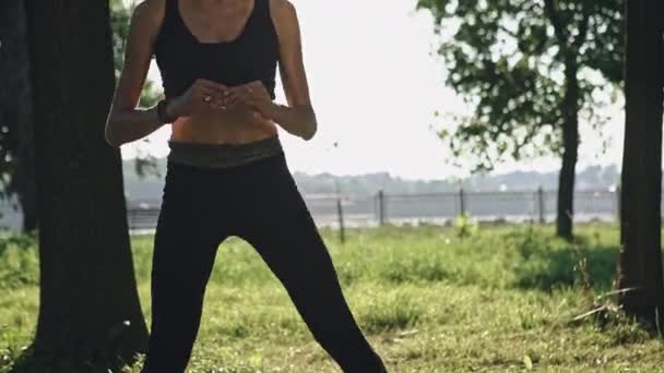 Jeune femme en vêtements de sport faisant de l'exercice dans le parc par une journée ensoleillée — Video