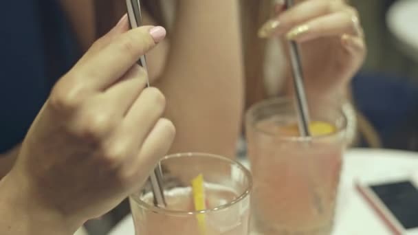 Duas mulheres bebendo coquetéis em um bar com uma inclinação para cima vista das bebidas e palhas para seus rostos . — Vídeo de Stock