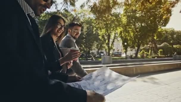 Трое бизнесменов идут вместе на улицу с самым близким к камере человеком, читая бумажный документ на видном месте . — стоковое видео