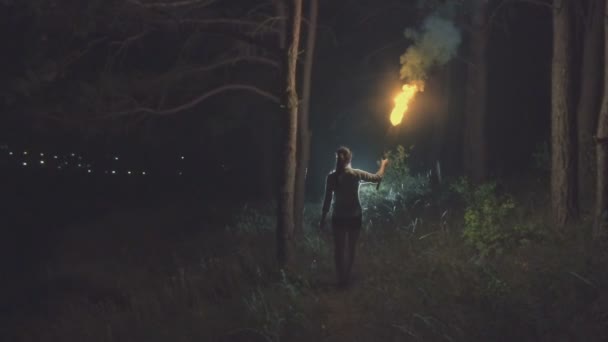 Mladá hezká holka v lese v noci obrácený stojan drží pochodeň a při pohledu na město. — Stock video