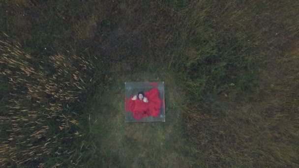 Uma jovem em um vestido de noite vermelho sentado em uma caixa de vidro, baleado de cima. Vista aérea . — Vídeo de Stock