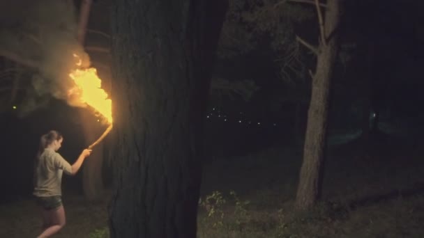 Une fille avec une torche enflammée à la main traverse la forêt la nuit. Mouvement lent . — Video