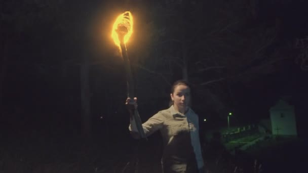 De vurige fakkel in de hand van een meisje lopen in de bossen van de verschrikkelijke nacht. Voor de kerk van de achtergrond met een kruis. Griezelig video. Slow motion — Stockvideo