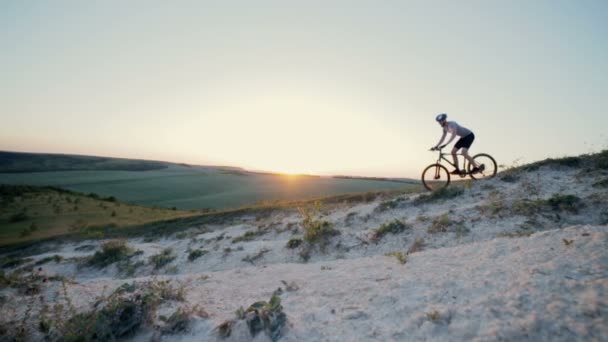 Велосипедист едет по пересеченной местности через низкие горы — стоковое видео