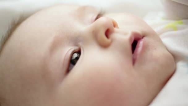De cerca en la cara de un adorable bebé recién nacido acostado en una manta moviendo sus manos a través de su boca — Vídeos de Stock
