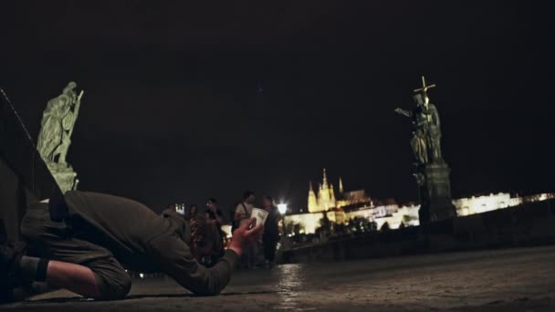 Vista lateral del pobre hombre pidiendo limosna a las personas que pasan por la calle con el fondo de la ciudad iluminada, Praga . — Vídeo de stock