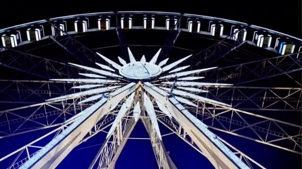 Roterande upplyst pariserhjul underifrån med passagerare gondoler upphängd på rim mot en natthimmel på en karneval eller sällskapsspel. — Stockvideo