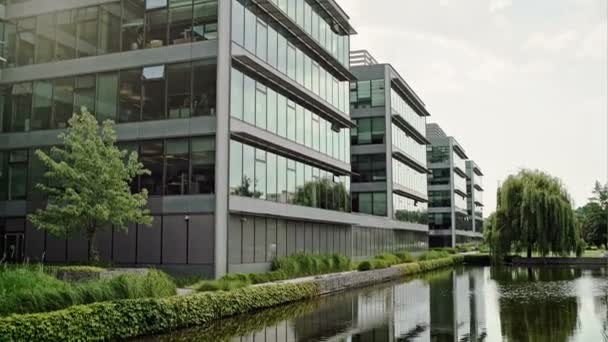 Modern office complex with glass fronted buildings in a scenic landscaped garden with pond ad reflections. — Stock Video