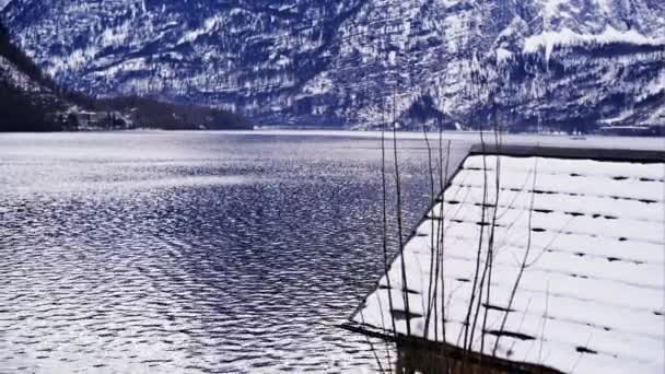 Χιονισμένη στέγη του σπιτιού τοποθετείται στην ακτογραμμή της λίμνης στο Χάλστατ, Αυστρία με τα βουνά στο φόντο — Αρχείο Βίντεο