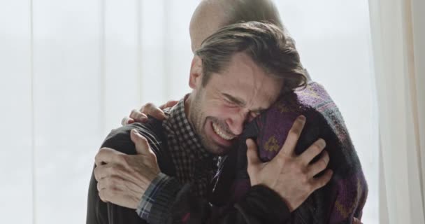 Vista laterale di senior abbracciare l'uomo adulto piangendo dalla felicità in piedi contro la finestra alla luce del sole . — Video Stock