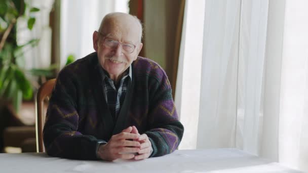 Gutaussehender, fröhlicher älterer Herr, der am Tisch im Wohnzimmer sitzt. Seniorenaktivität und Lifestyle-Konzept. — Stockvideo