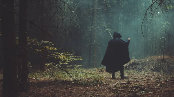 Un hombre con una capa negra en el bosque conoce a una chica y ambos huyen del bosque. La escena dramática para el día de Halloween — Foto de Stock