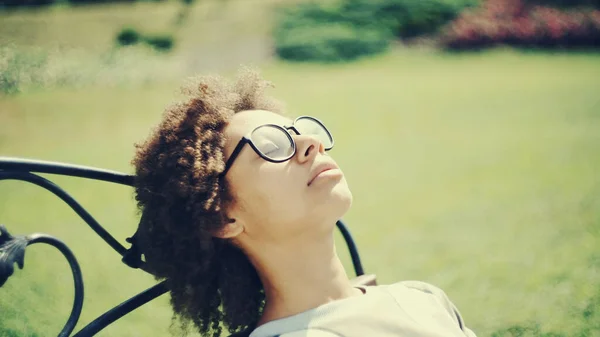 Chica joven sentada en un banco de un parque y respirando aire fresco profundo Fotos de stock