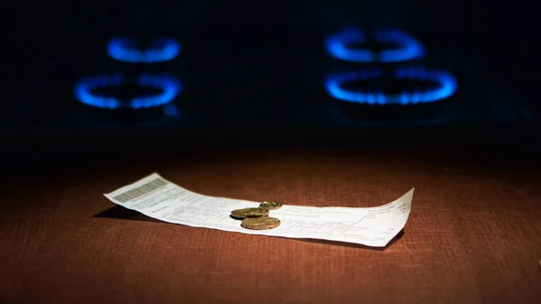 Счет за коммунальные услуги и монеты для оплаты на фоне сжигания газа на газовой плите — стоковое фото