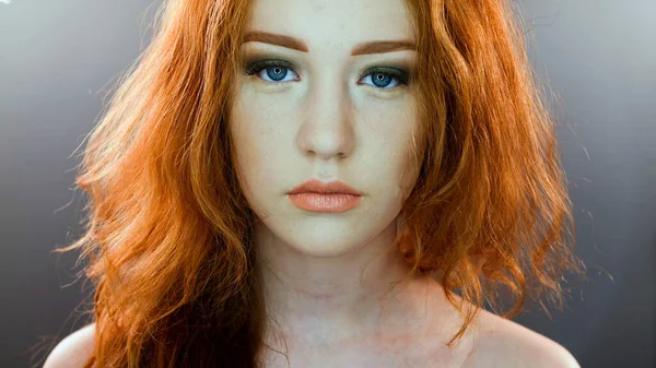 Bela adolescente com cabelo vermelho soprando e olhos azuis no fundo estúdio cinza — Fotografia de Stock