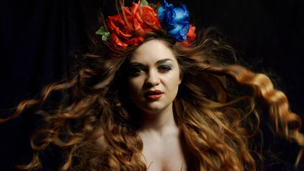 Beautiful women with a wreath of colors flowers sitting on a black background, close up — Stock Photo, Image