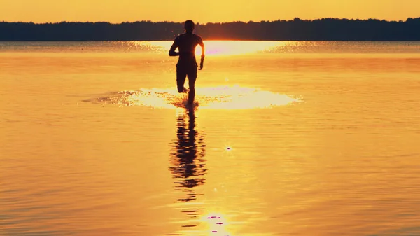 Oben ohne, athletischer, muskulöser und gesunder Mann, der im Wasser läuft und bei Sonnenuntergang Wasser spritzt — Stockfoto
