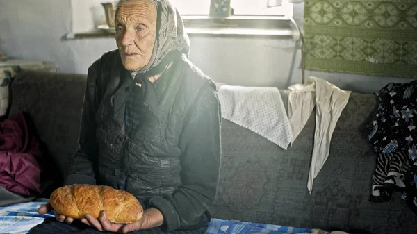 Pobre abuela sosteniendo pan en sus rodillas y su cabeza temblando desde la vejez Imagen de archivo