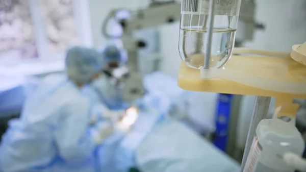 Team kirurger utför en åtgärd i en operationssal, ett dropp i förgrunden — Stockfoto
